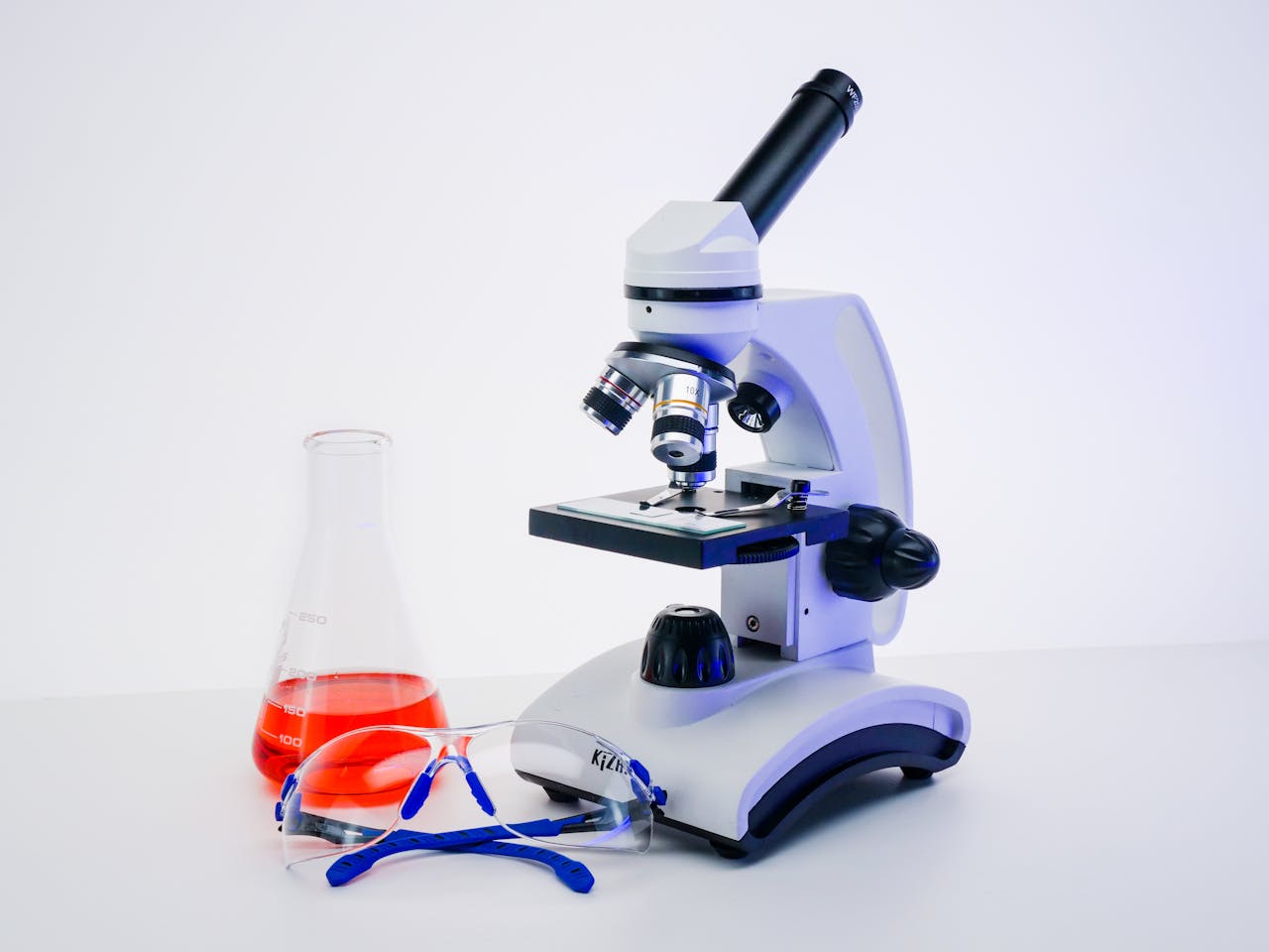 Microscope with Erlenmeyer flask and protective goggles in a science lab setting.
